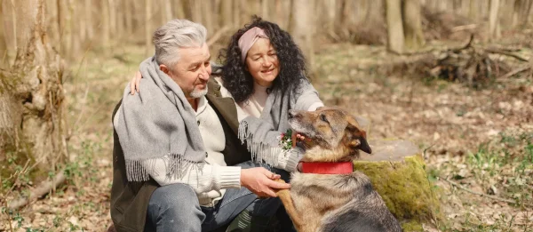Couple de seniors accroupi en forêt auprès d'un berger allemand
